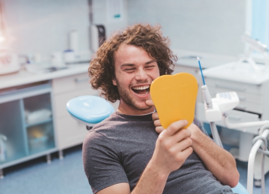 Young man in dental chair looking at his smile in mirror